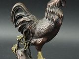 bronze statue of a rooster on a rock with a black background