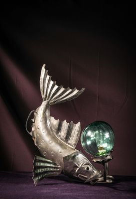 a silver fish statue with a green glass ball on a table