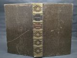 an old book sitting on top of a wooden table next to a gray wall