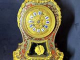 une horloge dorée et rouge posée sur un socle, sur fond bleu