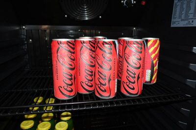 four cans of coca cola sitting on top of a rack in a refrigerator
