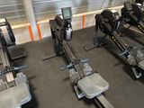 row of rowing machines in a gym with a monitor on the wall