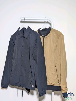 two jackets hanging on a clothes rack against a white wall
