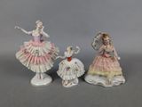 three porcelain figurines of women in dresses and holding umbrellas
