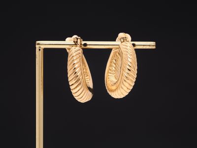 une paire de boucles d'oreilles en or posée sur un présentoir devant un fond noir