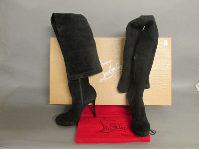 une paire de bottes noires en daim à talons hauts, posées sur une boîte rouge
