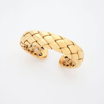 un gros plan d'un bracelet manchette en or sur fond blanc