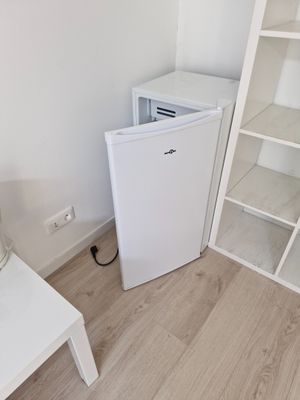 un petit réfrigérateur blanc dans le coin d'une pièce