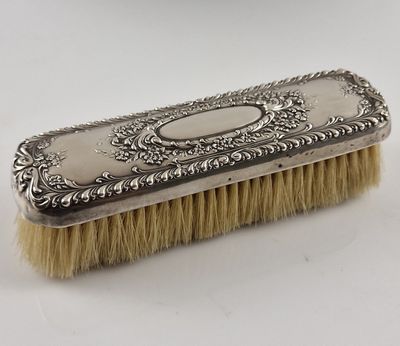 une brosse plaquée argent avec un manche, posée sur une surface blanche