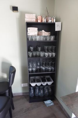 des bouteilles et des verres posés sur une étagère dans une pièce où se trouve une chaise noire