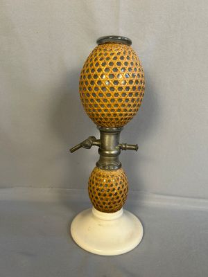 une lampe à huile à l'ancienne posée sur un socle blanc orné d'un motif jaune et noir