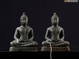 deux statues de bouddhas assis sur une surface noire