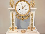 une horloge blanche et dorée posée sur un socle en bois