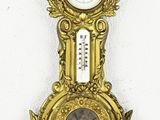 une horloge dorée accrochée au mur, sur laquelle se trouve un thermomètre