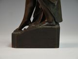 bronze statue of a woman sitting on a rock with her hands on her knees