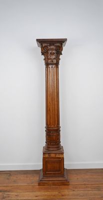 Une grande colonne en bois se dresse dans une pièce au sol recouvert de parquet.