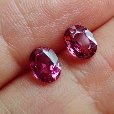 pair of pink tourmaline gems sitting on top of a person ' s finger