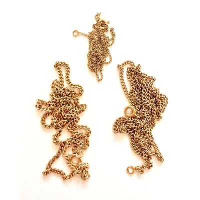 deux chaînes en or et un collier posés sur une surface blanche