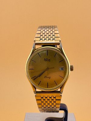 une image représentant une montre-bracelet en or posée sur un socle, sur fond jaune