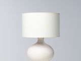 La lampe de table est blanche ; elle est dotée d'un pied en bois et d'un abat-jour blanc.