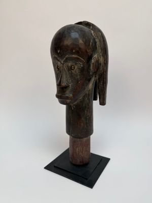 une sculpture en bois représentant la tête d'une femme, posée sur un socle noir
