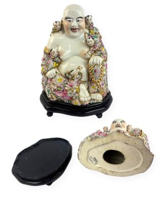 une statue représentant un Bouddha souriant, assis sur une chaise à côté d'un bougeoir