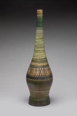 un vase vert et marron posé sur une surface blanche