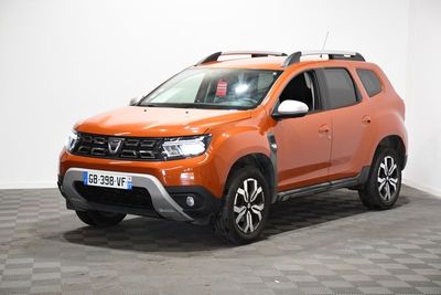 La Dacia orange est garée dans une pièce au sol carrelé en damier.