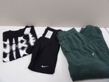 Trois paires de pantalons Nike et un t-shirt sont posés sur une table
