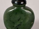 a green glass bottle with a black lid on a white surface