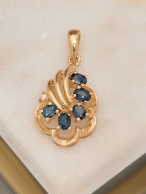 an image of a gold pendant with blue sapphires on a marble surface