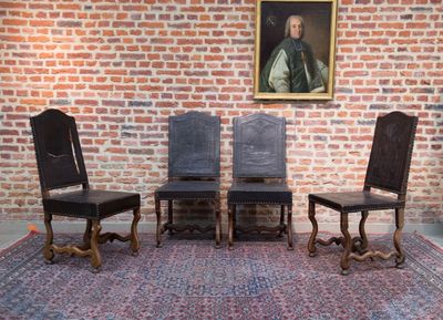 quatre chaises devant un mur de briques sur lequel est accrochée une peinture