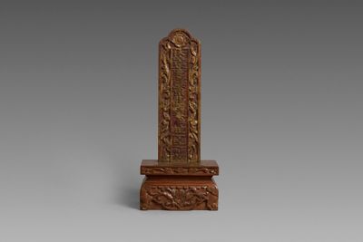 une image représentant un obélisque en bois sculpté posé sur une surface grise