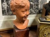un buste représentant un garçon assis à côté d'une horloge posée sur une table