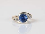 une photo d'une bague sertie d'un saphir bleu et de diamants, posée sur une surface blanche