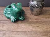 a green frog sitting on a table next to a silver container