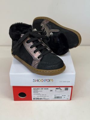 une paire de chaussures noires et roses, doublées de fourrure, posées sur une boîte