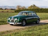 une vieille voiture verte qui roule sur une route longeant un champ verdoyant