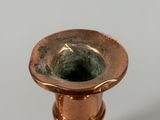 a small copper candle holder on a white surface