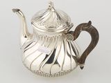 an antique silver teapot with a wooden handle on a white surface