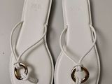 pair of white sandals with a gold ring on them on a white surface