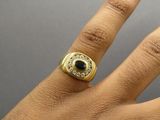 a man ' s hand with a gold ring with a black stone on it