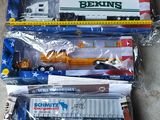 Plusieurs camions miniatures sont alignés dans des sacs en plastique posés par terre.