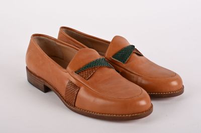 a pair of brown shoes with a green ribbon on the side