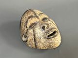 une image représentant un masque en pierre sur une surface grise
