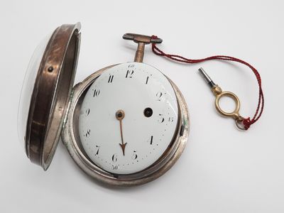 une montre de poche en argent posée sur une table, avec une clé