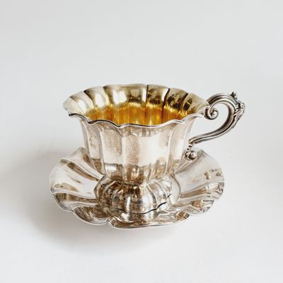 a silver cup and saucer sitting on a saucer