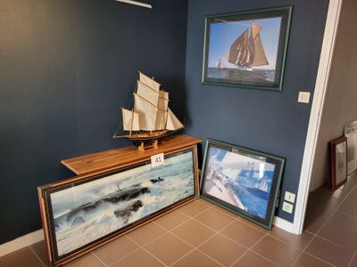 deux tableaux accrochés au mur, à côté d'une table sur laquelle est posé un bateau