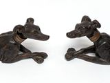 pair of bronze figurines of two dogs laying down on a white surface