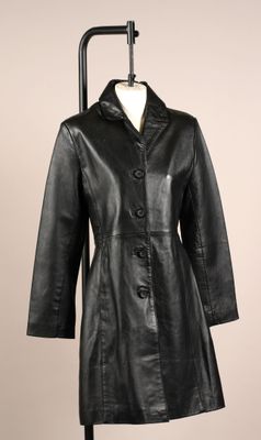 un manteau en cuir noir posé sur un mannequin, devant un mur beige